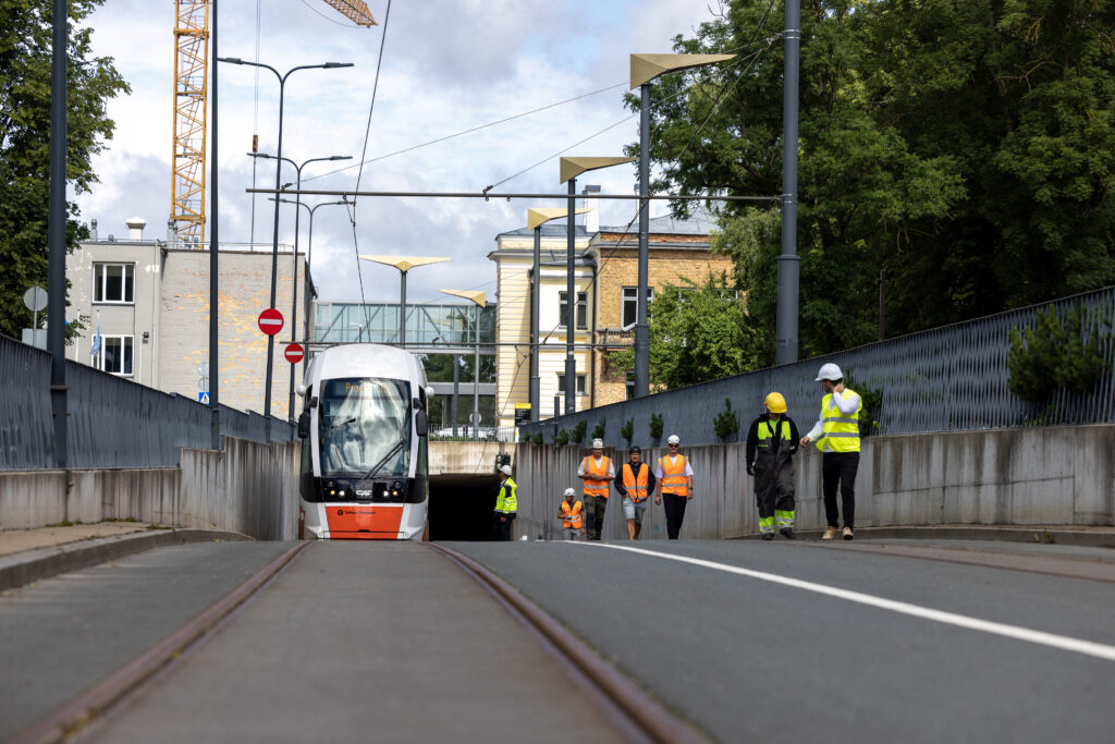 Valge tramm väljub tunnelist, paremal kõnnivad teel ehitustöölised.