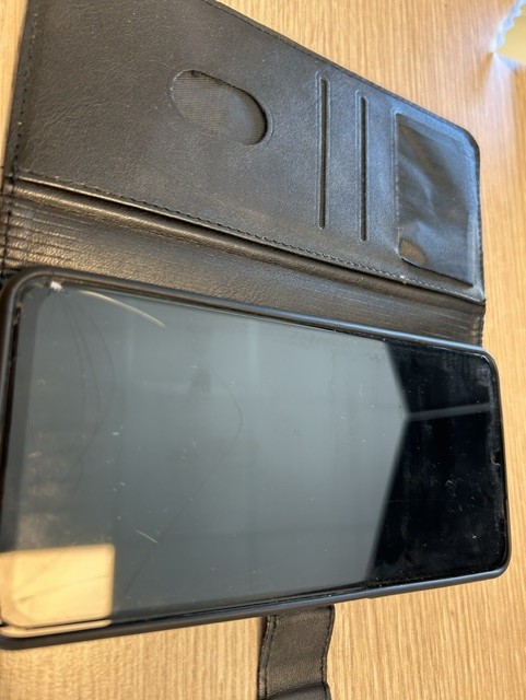 Must nutitelefon avatud mustas rahakotiümbrises puitpinnal, ekraan välja lülitatud.