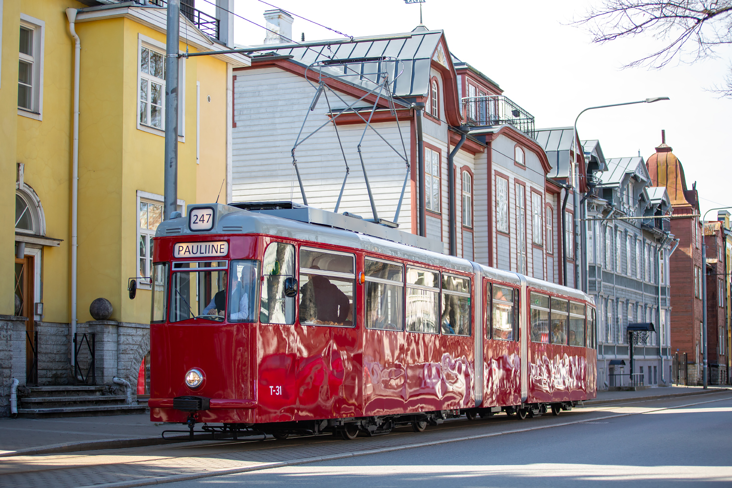 Ajalooline punane tramm sõidab Tallinna tänaval, taustal värvilised puumajad.