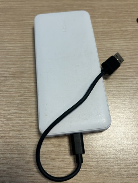 Valge akupank, mille külge on ühendatud must USB-kaabel, lamab heledal puitpinnal.