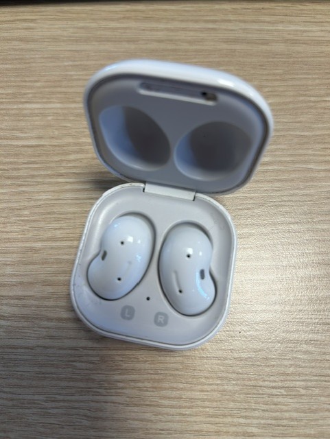 Valged Samsung Galaxy Buds Live juhtmevabad kõrvaklapid avatud laadimiskarbis puitpinnal.