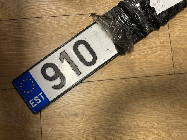 Eesti numbrimärk numbritega 910, osaliselt musta kilega pakitud, lamab puitpõrandal.